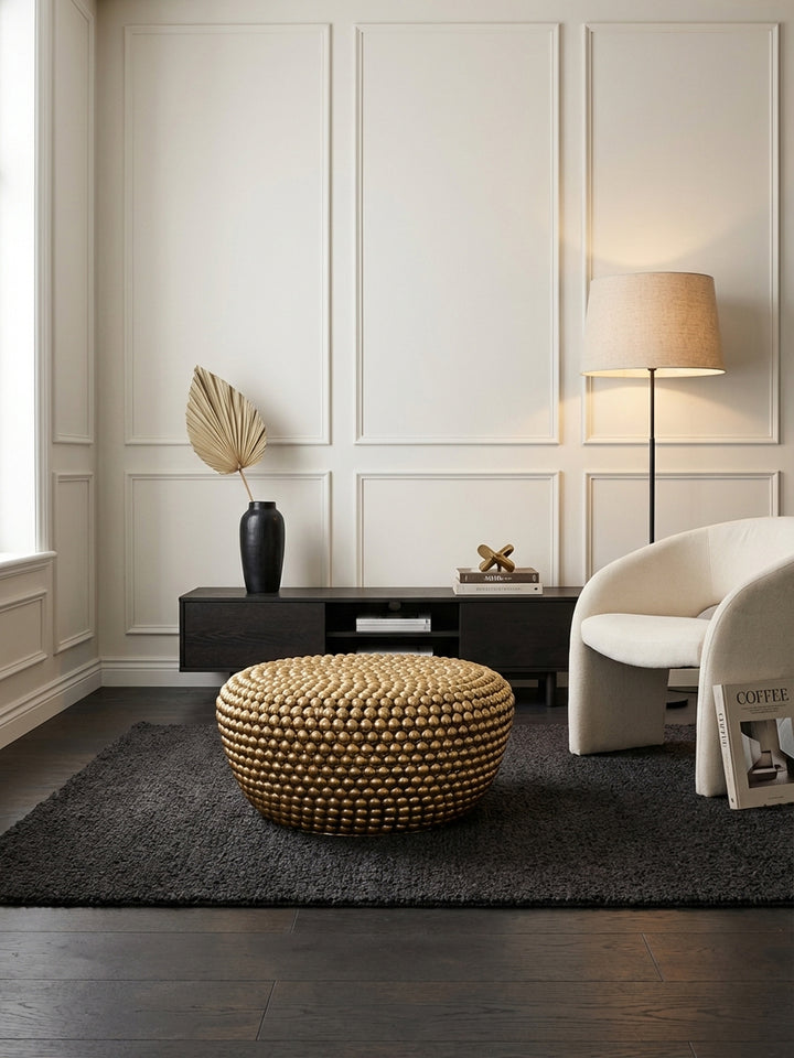 Eleganter runder Couchtisch in Gold als Blickfang in einem modern-klassischen Wohnzimmer, platziert auf einem dunklen Teppich vor einem Ledersofa._