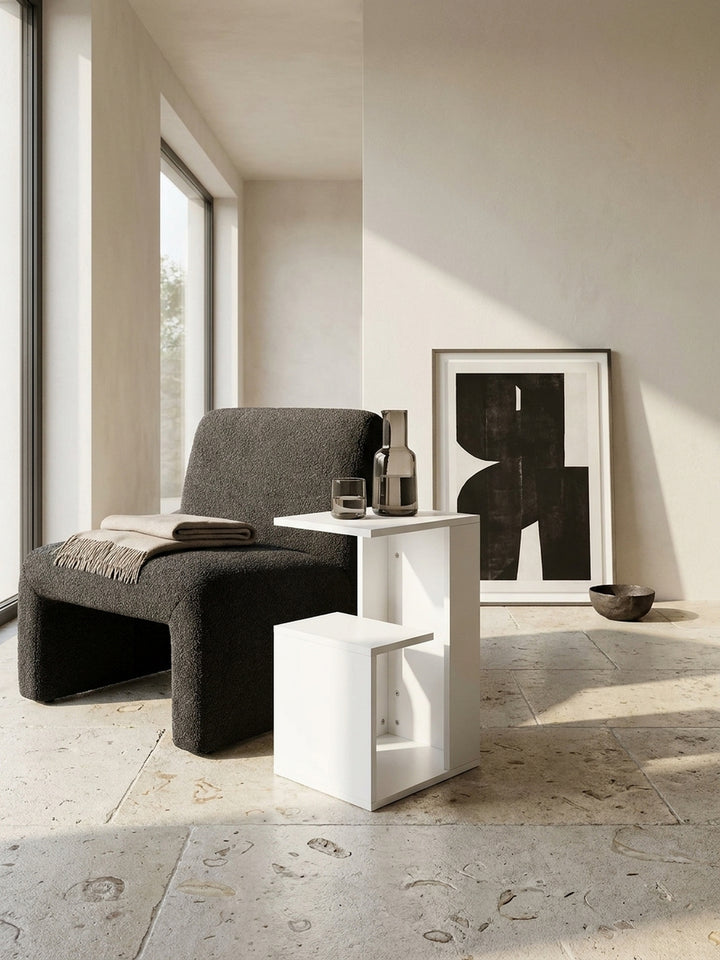 Weißer C-Form Sofatisch im architektonischen Zusammenspiel mit einem dunklen Bouclé-Sessel und einer dezent fließenden Kaschmirdecke_