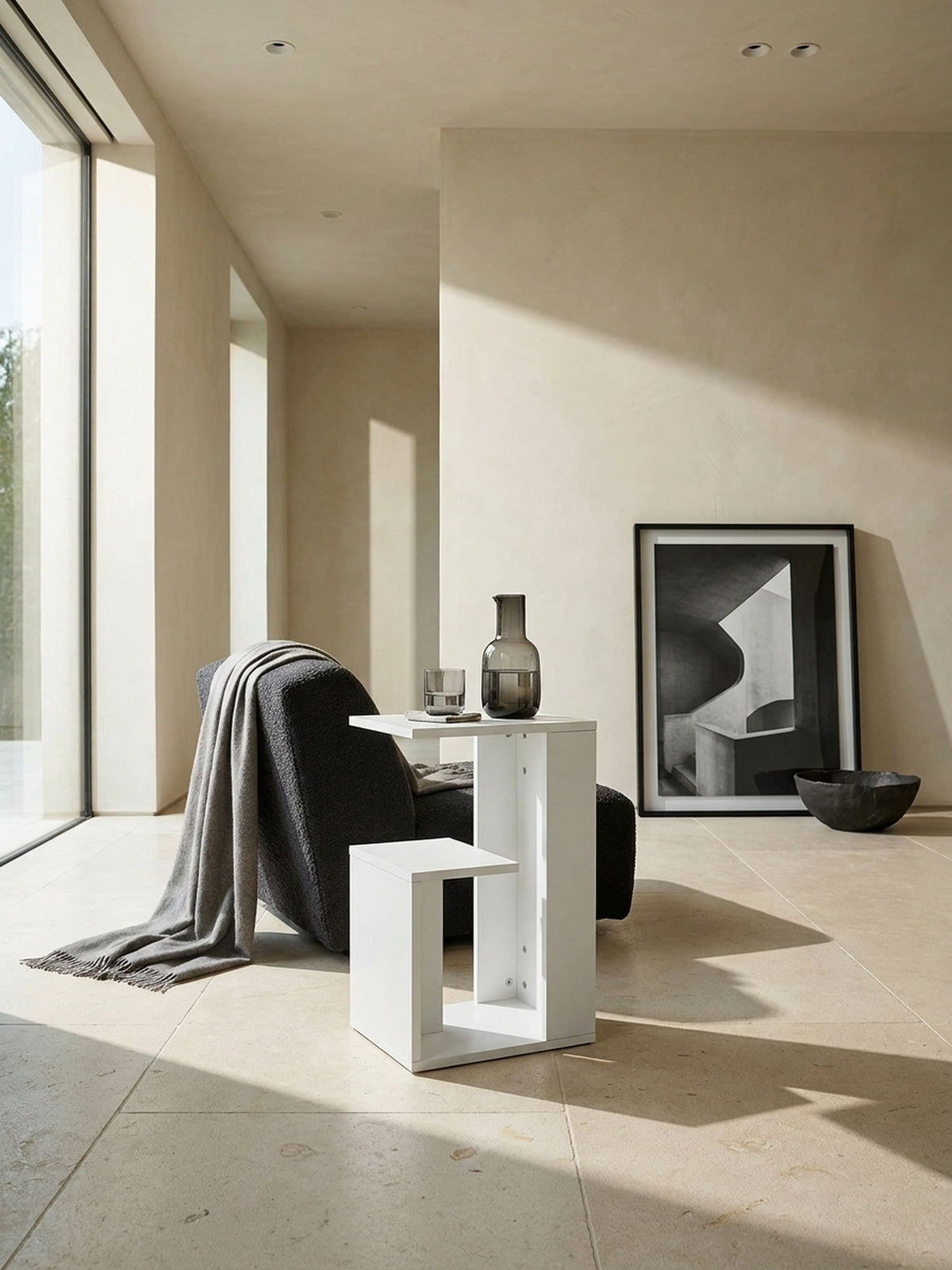 Minimalistischer Beistelltisch in Weiß 35x30x61 cm als abstrakter Kontrast neben einem anthrazitfarbenen Lounge-Sessel auf edlem Kalksteinboden_