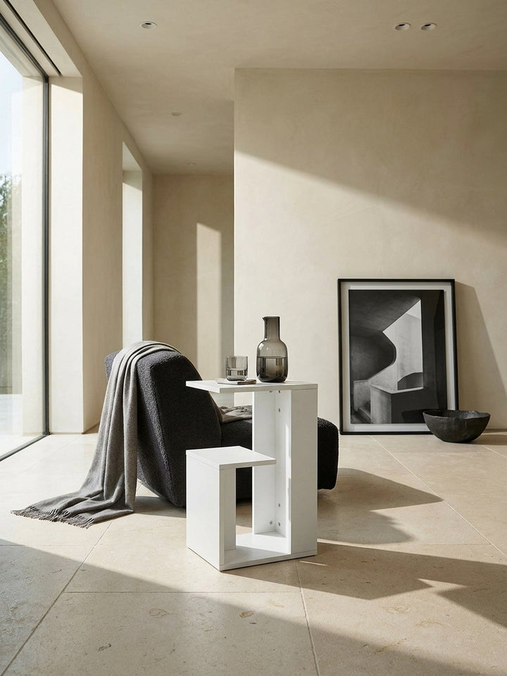 Minimalistischer Beistelltisch in Weiß 35x30x61 cm als abstrakter Kontrast neben einem anthrazitfarbenen Lounge-Sessel auf edlem Kalksteinboden_