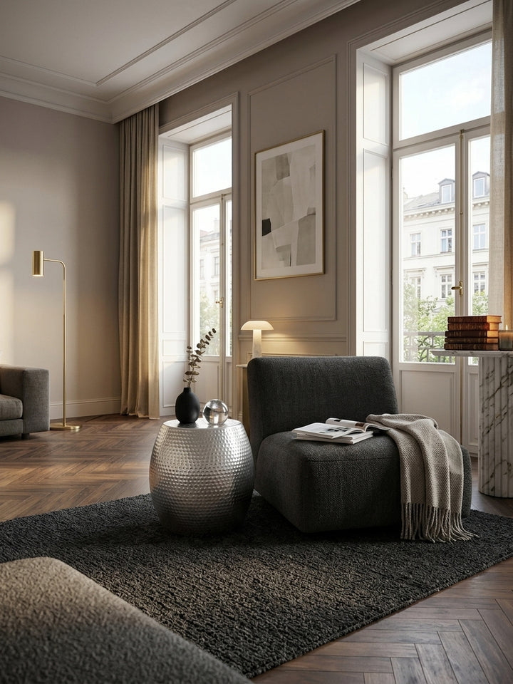 Silberner Aluminium Beistelltisch im edlen Wohnzimmer. Der orientalische Hammerschlag Couchtisch glänzt neben einem dunklen Sessel auf hochwertigem Walnussparkett._