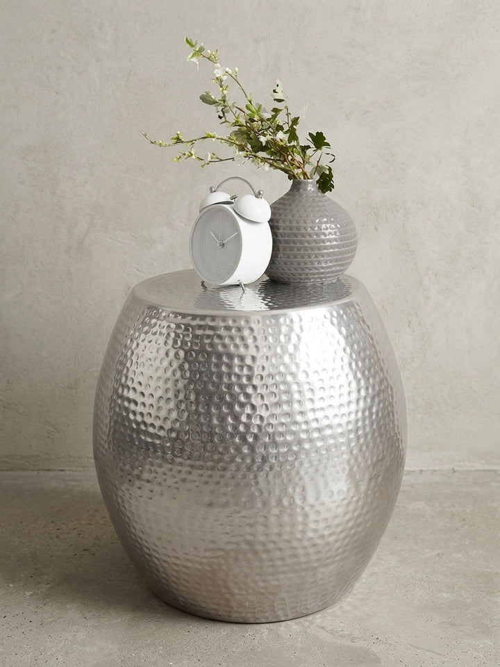 Freigestellter Aluminium Beistelltisch in Silber. Die bauchige, runde Silhouette des orientalischen Metalltisches zeigt das markante, glänzende Hammerschlag-Muster._