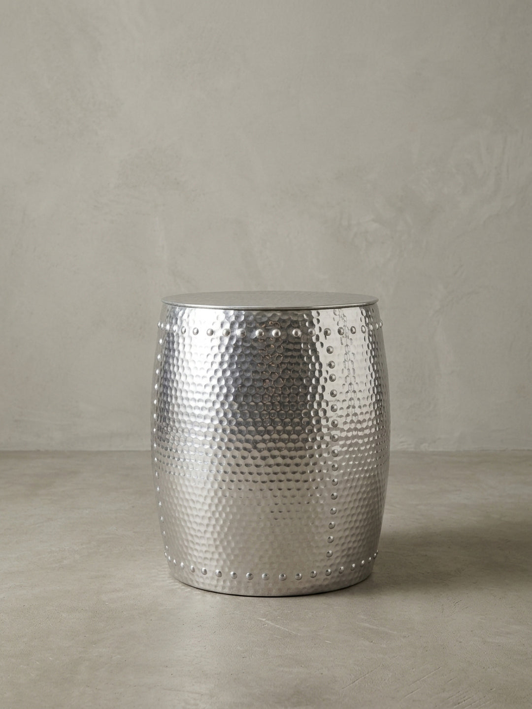 Alternative Perspektive auf den glänzenden Aluminiumtisch. Das einfallende Licht betont die plastischen Reliefs und das orientalische Muster des kleinen runden Abstelltisches._