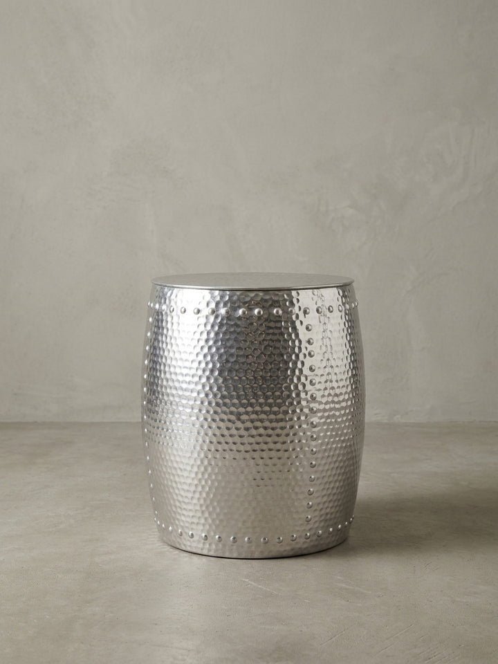 Alternative Perspektive auf den glänzenden Aluminiumtisch. Das einfallende Licht betont die plastischen Reliefs und das orientalische Muster des kleinen runden Abstelltisches._
