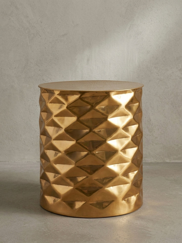 Im Dreiviertelprofil entfaltet der orientalisch anmutende Couchtisch aus Aluminium seine volle räumliche Tiefe, wobei das goldene Finish elegante Glanzpunkte auf der glatten Oberfläche setzt._