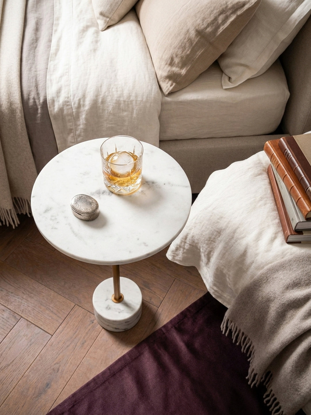 Draufsicht auf den runden Beistelltisch aus Marmor, platziert auf einem Holzboden neben einem beigen Sofa und einem geflochtenen Korb._