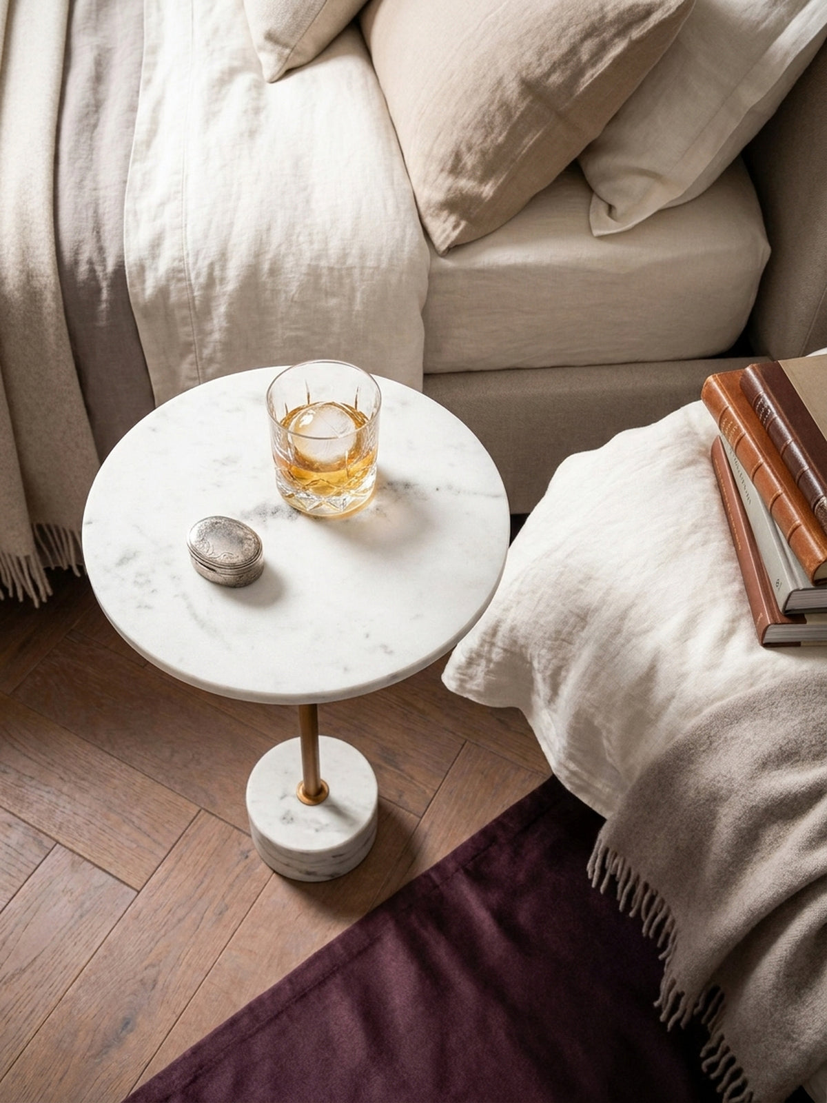 Draufsicht auf den runden Beistelltisch aus Marmor, platziert auf einem Holzboden neben einem beigen Sofa und einem geflochtenen Korb._