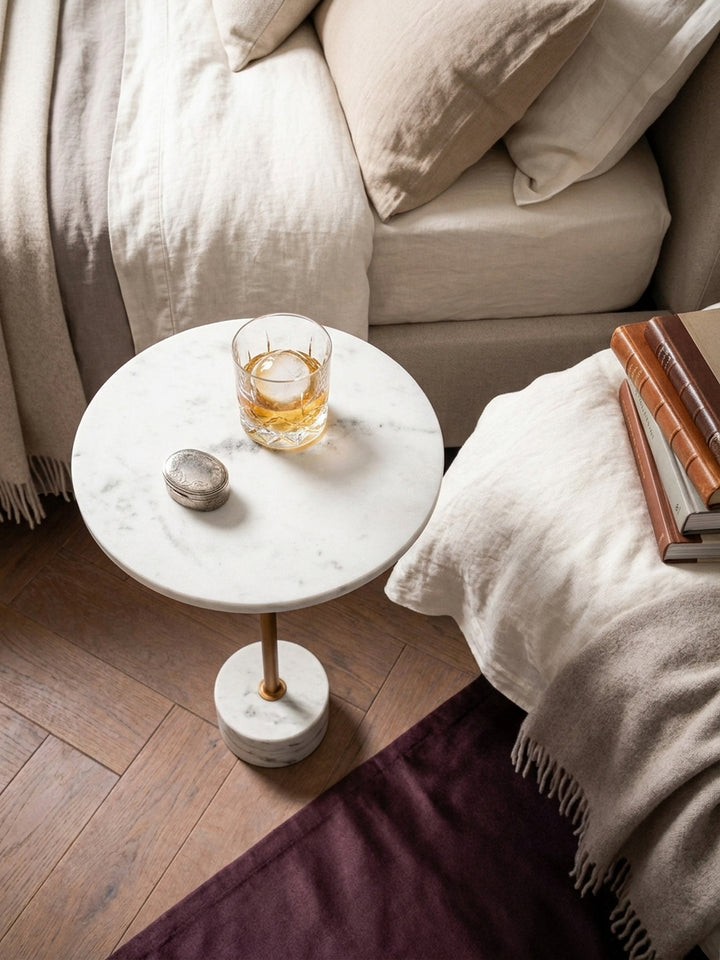 Draufsicht auf den runden Beistelltisch aus Marmor, platziert auf einem Holzboden neben einem beigen Sofa und einem geflochtenen Korb._