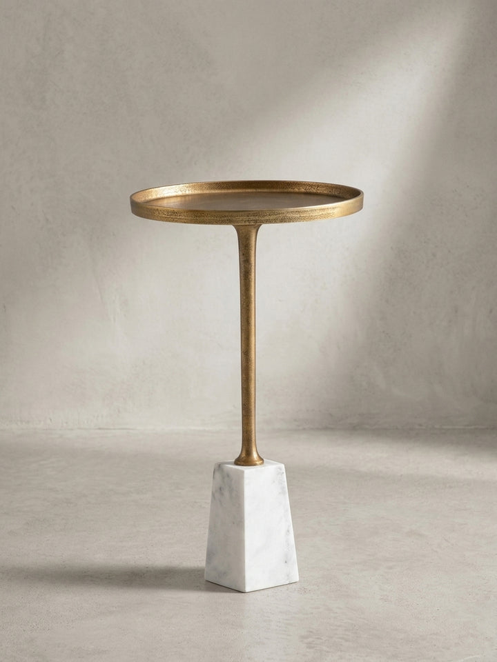 Moderner Beistelltisch aus der Dreiviertelperspektive, der die elegante Verbindung von goldenem Metallstiel und Marmorbasis zeigt._