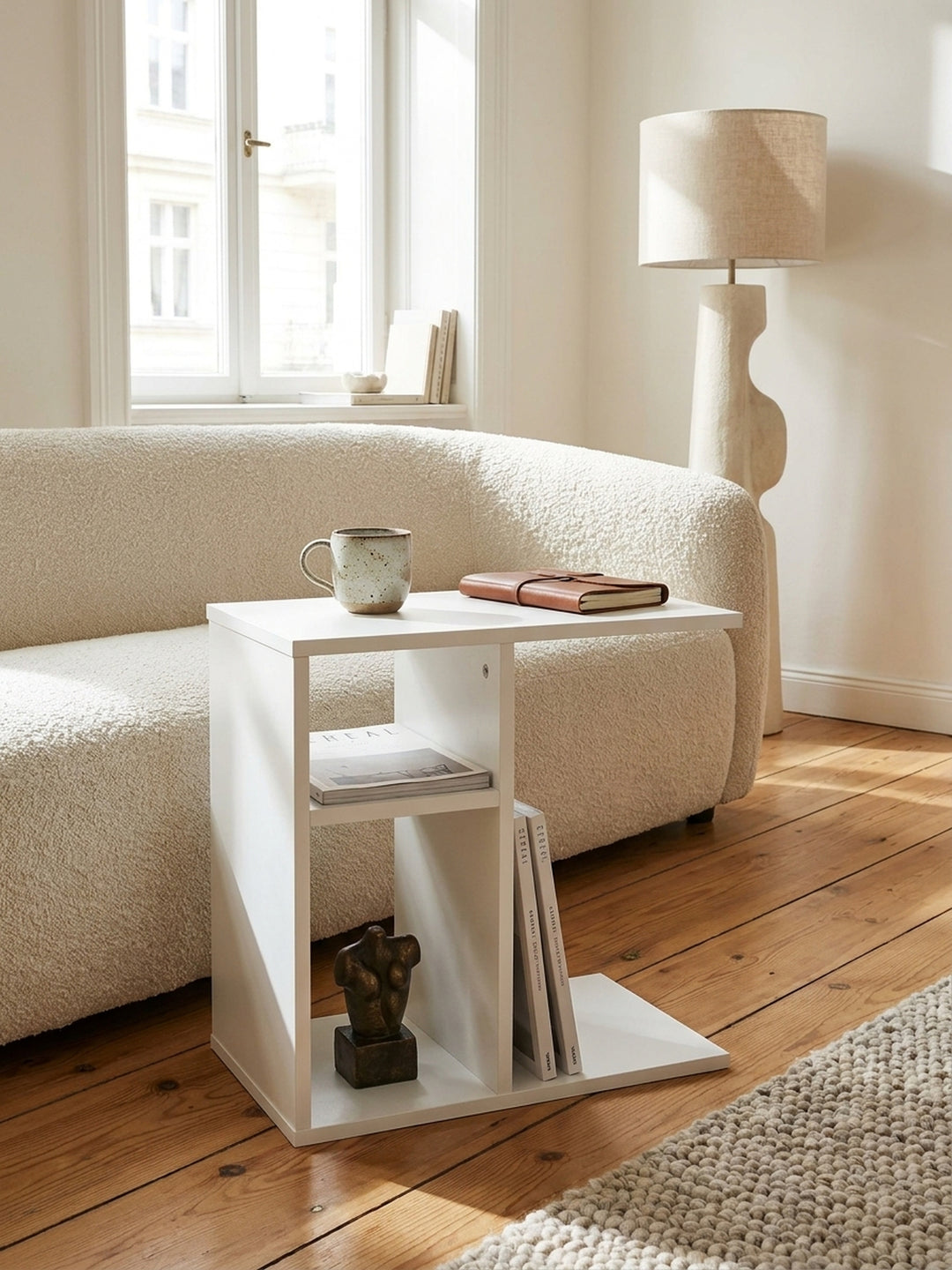 Nahaufnahme der glatten mattweißen Oberfläche des praktischen Couchtischs neben weichen Bouclé-Kissen und einer Keramiktasse._