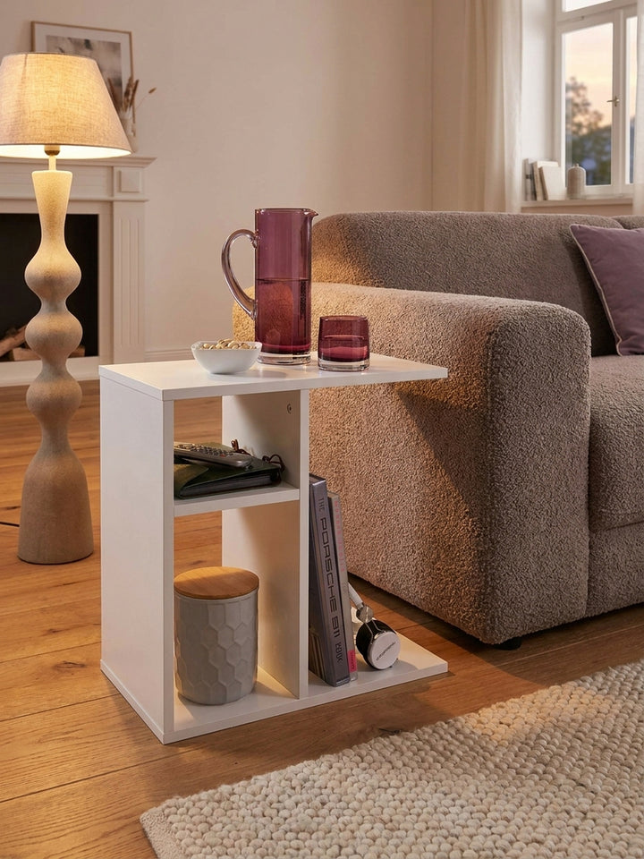 Schmaler Wohnzimmertisch in C-Form liebevoll dekoriert mit Magazinen im Ablagefach unter einer eleganten Leinenschirm-Stehleuchte._