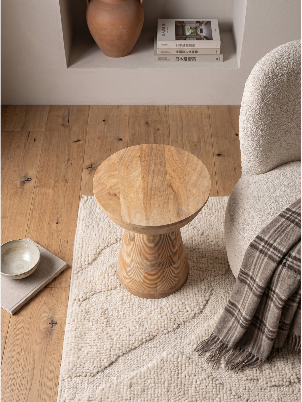 Draufsicht auf den runden Holztisch aus natürlichem Mango Massivholz im modernen Wohnbereich, arrangiert mit einer skulpturalen Stehlampe und einem hellen Sessel auf edlem Eichenparkett