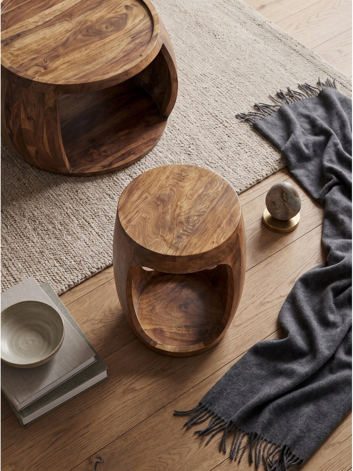 Blick von oben auf den runden Holz-Couchtisch mit offenem Fach im organisch modernen Wohnkonzept auf beigem Wollteppich_