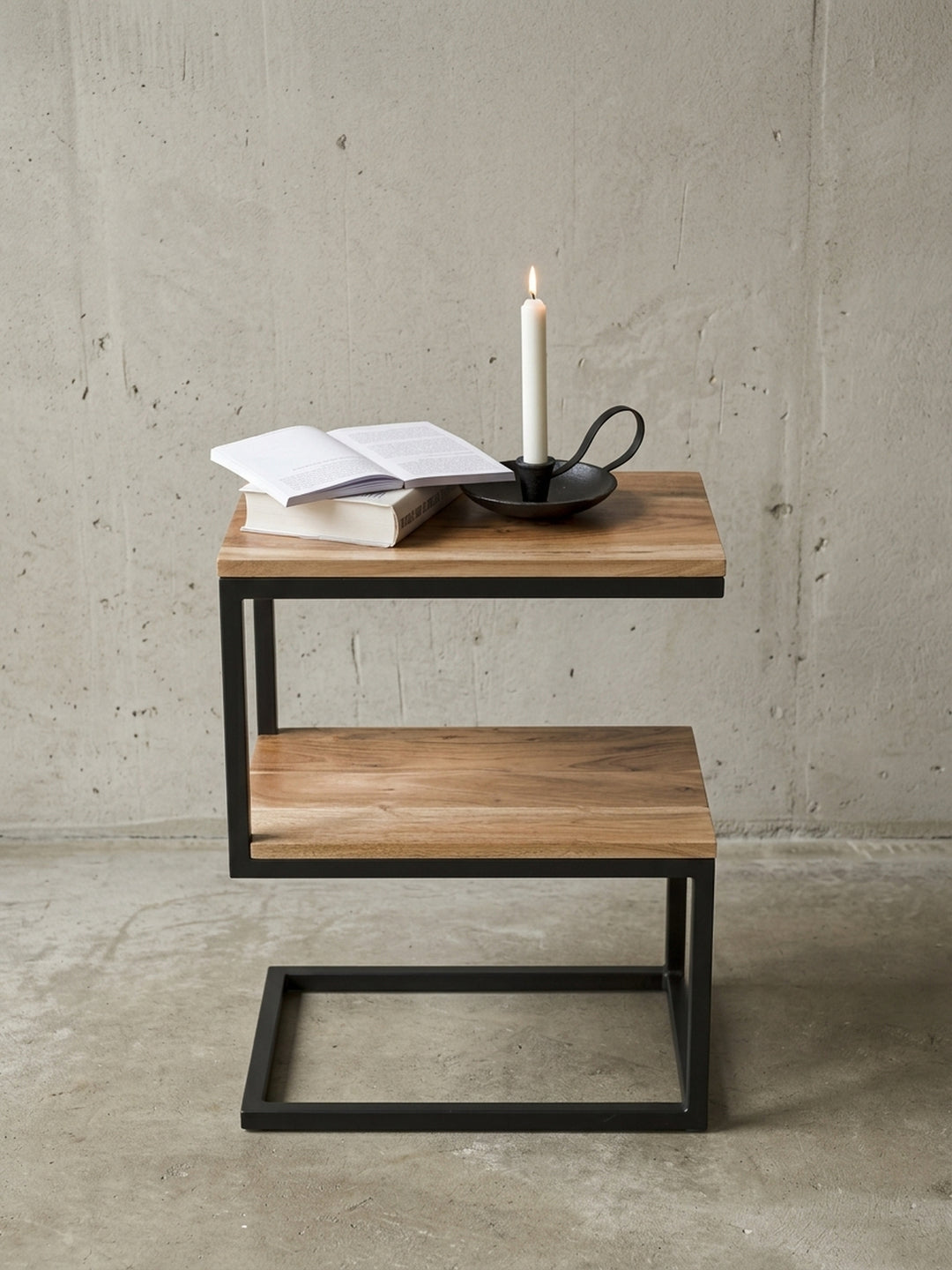 Nahaufnahme der Materialverbindung beim S-Form Beistelltisch. Das warme Akazienholz liegt passgenau im pulverbeschichteten schwarzen Metallrahmen des Landhaus-Stil Tisches._