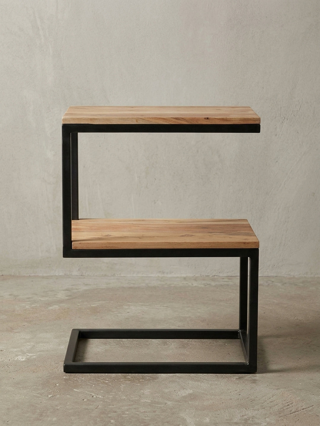 Freigestellter Beistelltisch in markanter S-Form. Das schwarze Metallgestell und die zwei Ablageflächen aus massivem Akazienholz zeigen klares Design für moderne Wohnzimmer._