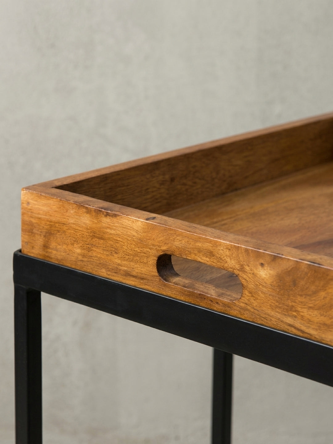 Fokus auf die präzise gearbeiteten Griffmulden des Serviertisches. Die Kombination aus warmem Sheesham Massivholz und dem kühlen, mattschwarzen Metallrahmen wirkt äußerst hochwertig._