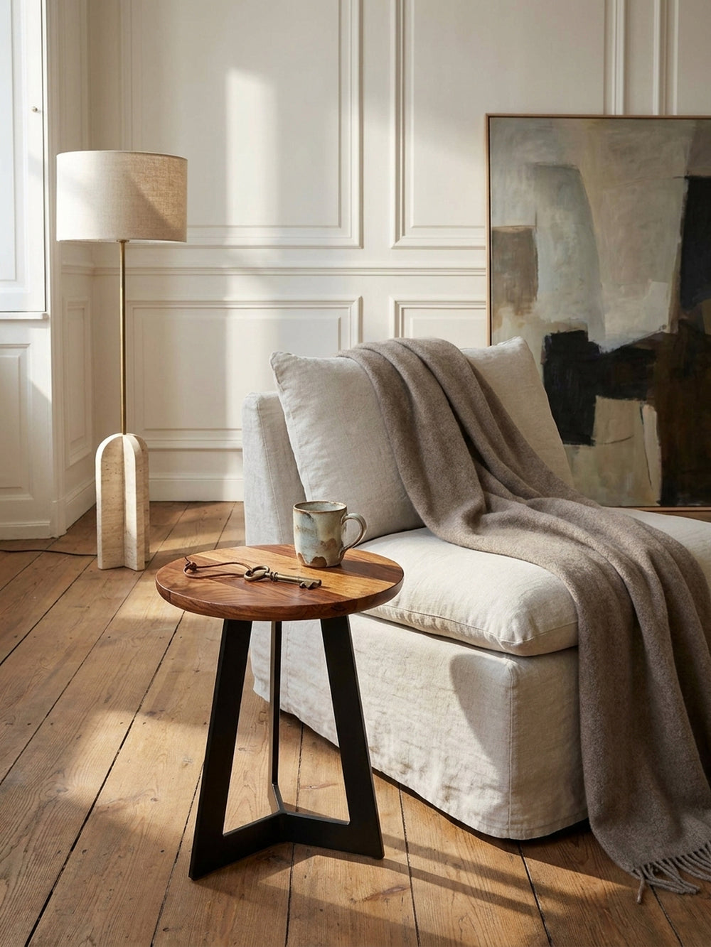 Massiver Holz-Beistelltisch im Industrie-Design arrangiert neben einem tiefen Lounge-Sessel mit drapiertem Kaschmirplaid vor einer warmweißen Wand._