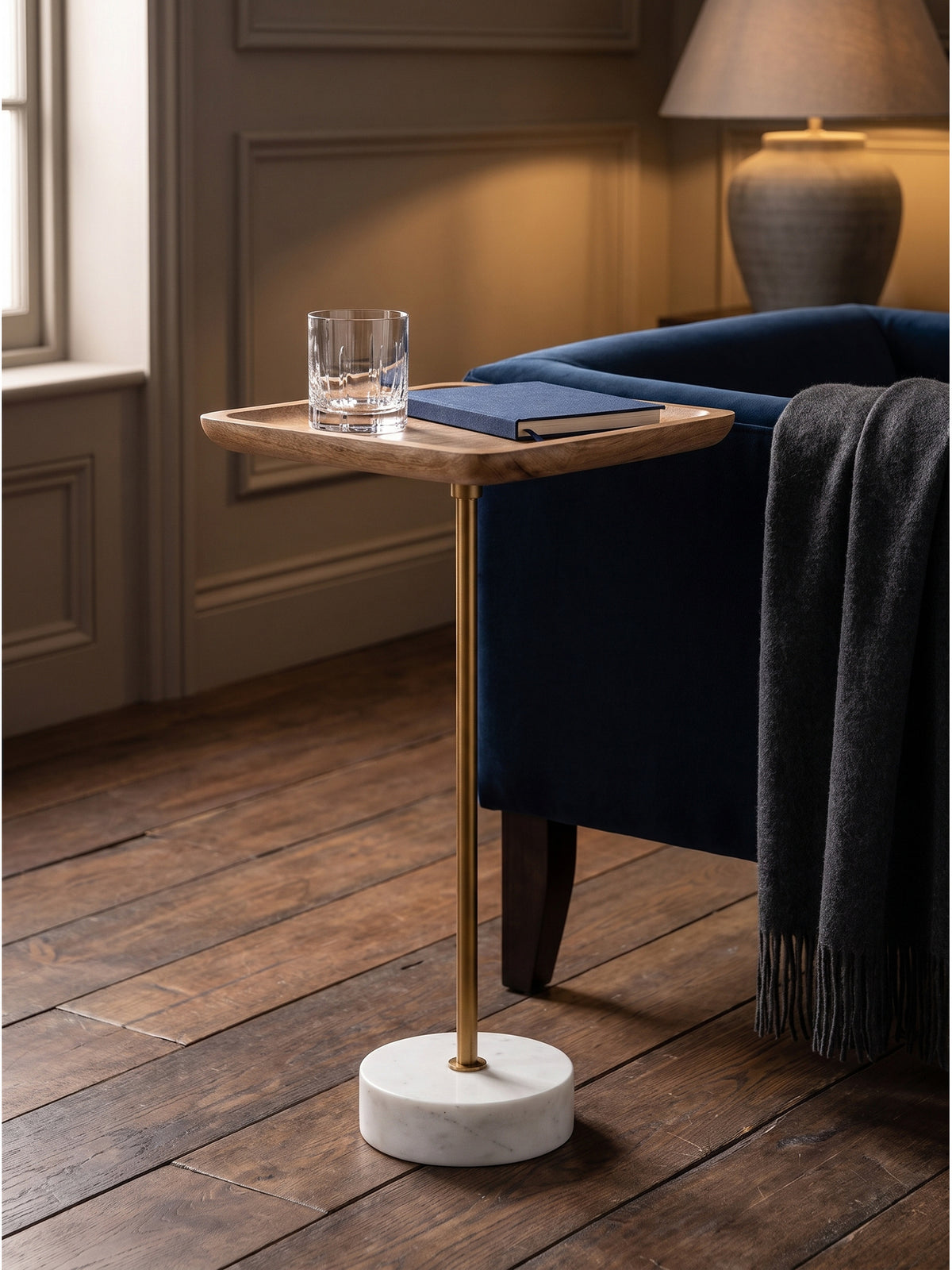 Kleiner Anstelltisch 55cm hoch mit einem Kristallglas-Tumbler und Buch stimmungsvoll arrangiert im gemütlichen abendlichen Lesebereich._