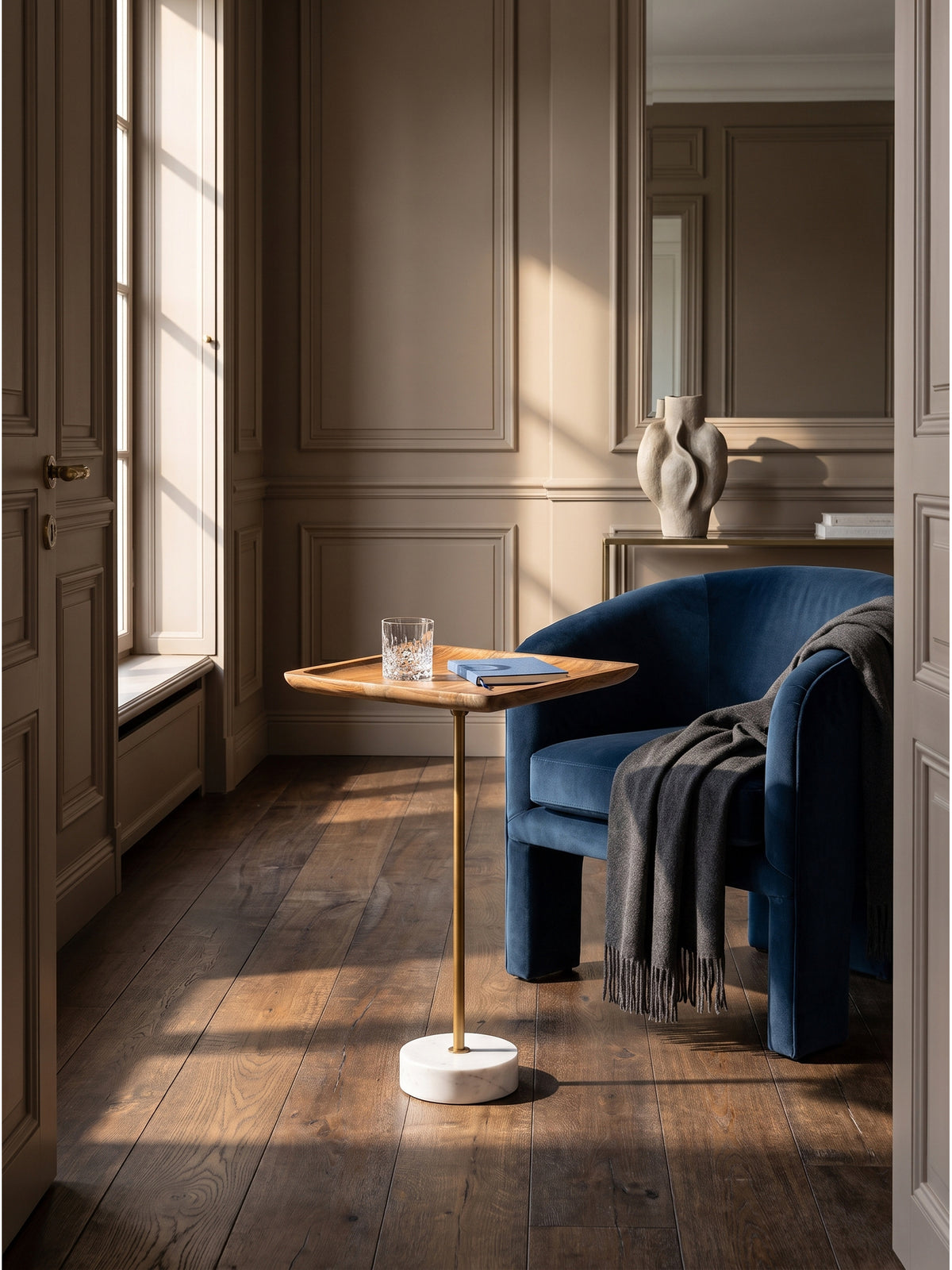 Eleganter Beistelltisch aus warmem Mango Massivholz mit goldener Mittelsäule im klassisch modernen Wohnzimmer vor einer greige gestrichenen Wand.