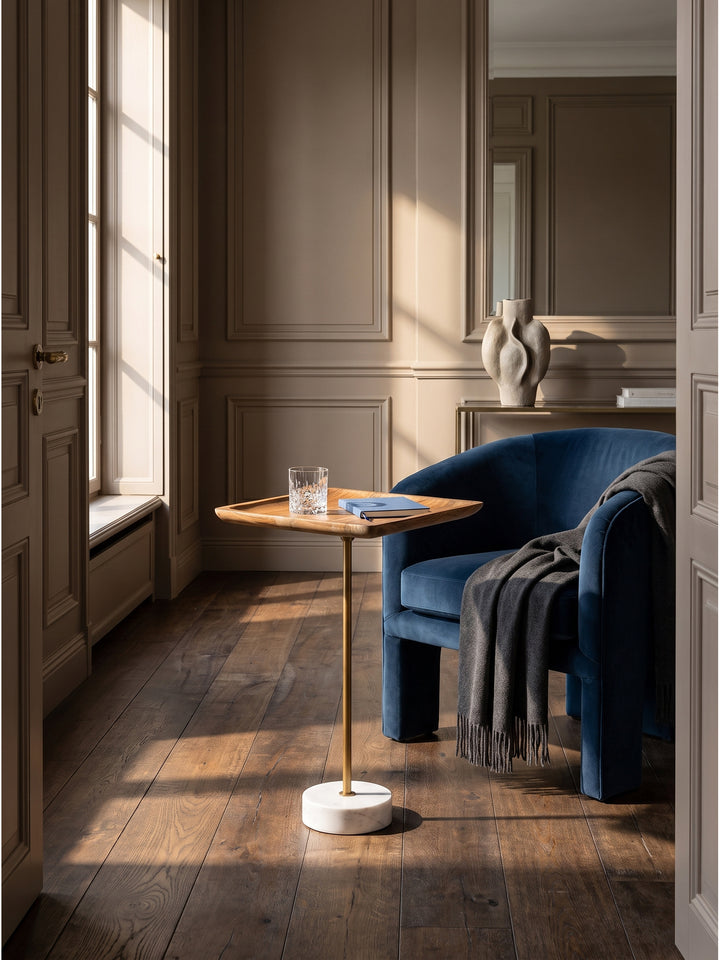 Eleganter Beistelltisch aus warmem Mango Massivholz mit goldener Mittelsäule im klassisch modernen Wohnzimmer vor einer greige gestrichenen Wand._