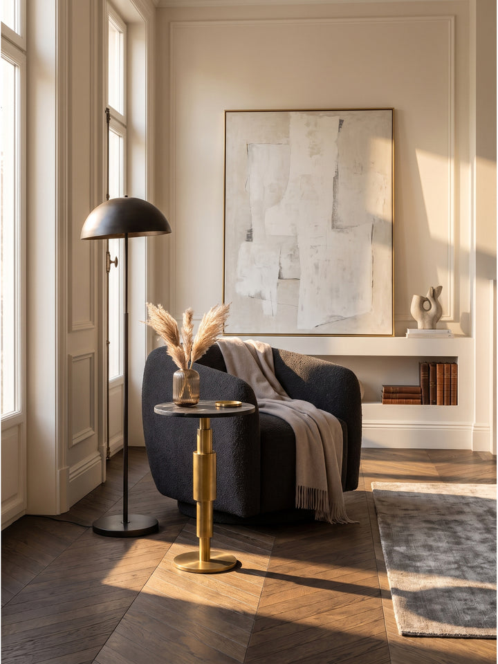 Eleganter Beistelltisch mit schwarzer Marmorplatte im eleganten Wohnzimmer auf dunklem Fischgrätparkett neben einem Sessel_