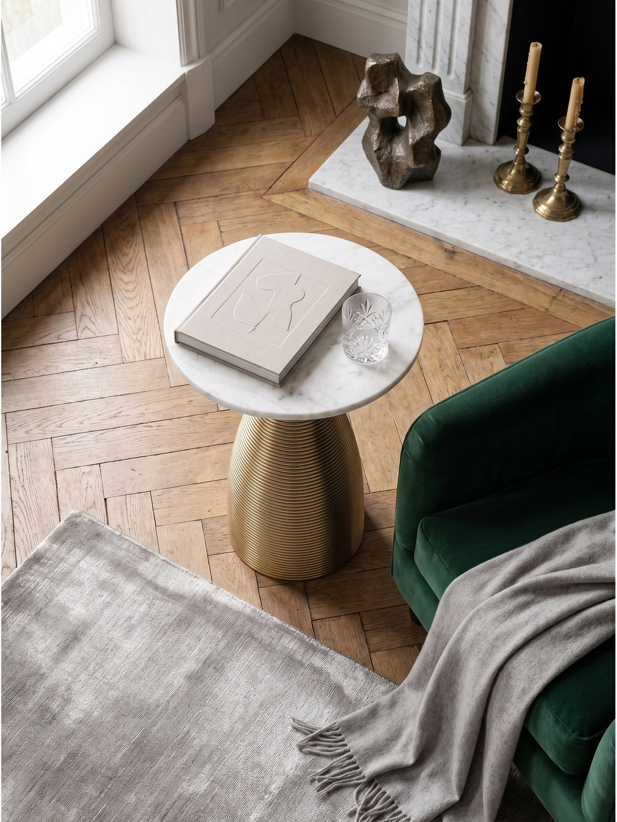Draufsicht auf den runden Naturstein Couchtisch mit geriffelter Goldbasis auf dunklem Fischgrätparkett im eleganten Loungebereich_