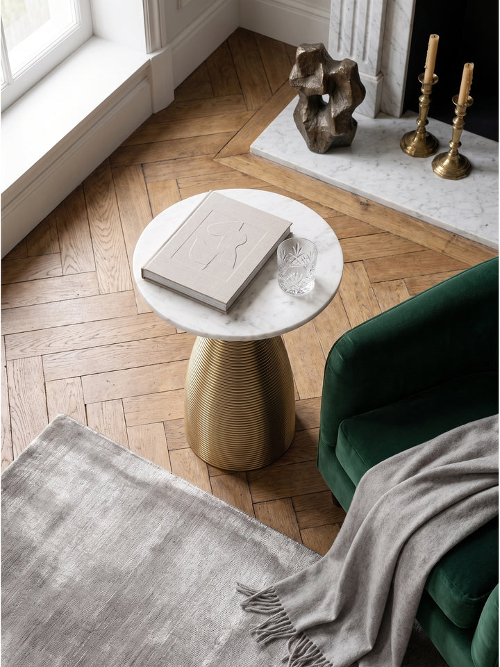 Draufsicht auf den runden Naturstein Couchtisch mit geriffelter Goldbasis auf dunklem Fischgrätparkett im eleganten Loungebereich_