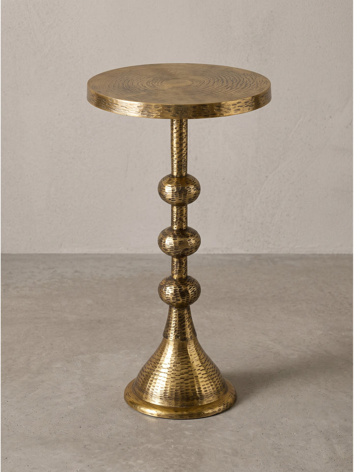 Runder Beistelltisch aus massivem Aluminium in Antik-Gold mit charakteristischem Säulenfuß und drei kugelförmigen Elementen auf weißem Hintergrund._
