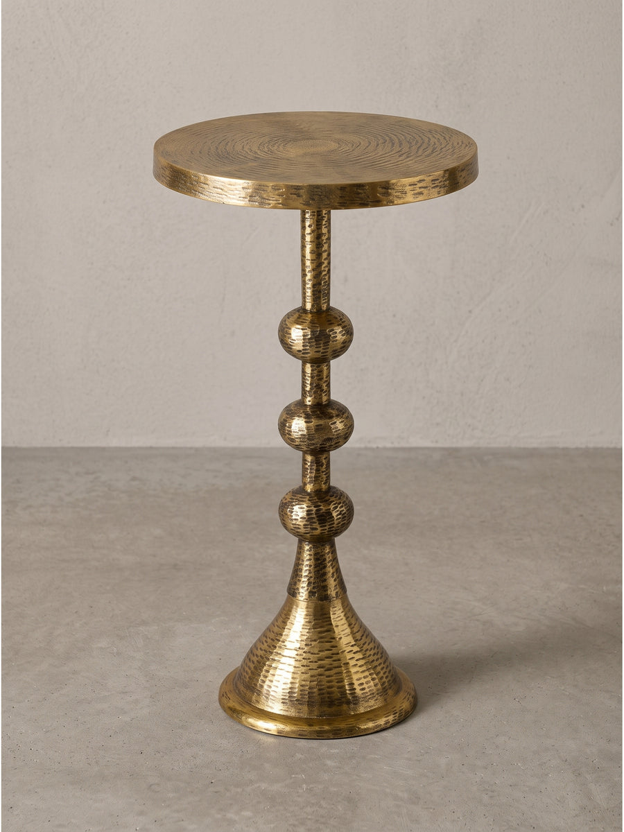 Runder Beistelltisch aus massivem Aluminium in Antik-Gold mit charakteristischem Säulenfuß und drei kugelförmigen Elementen auf weißem Hintergrund._