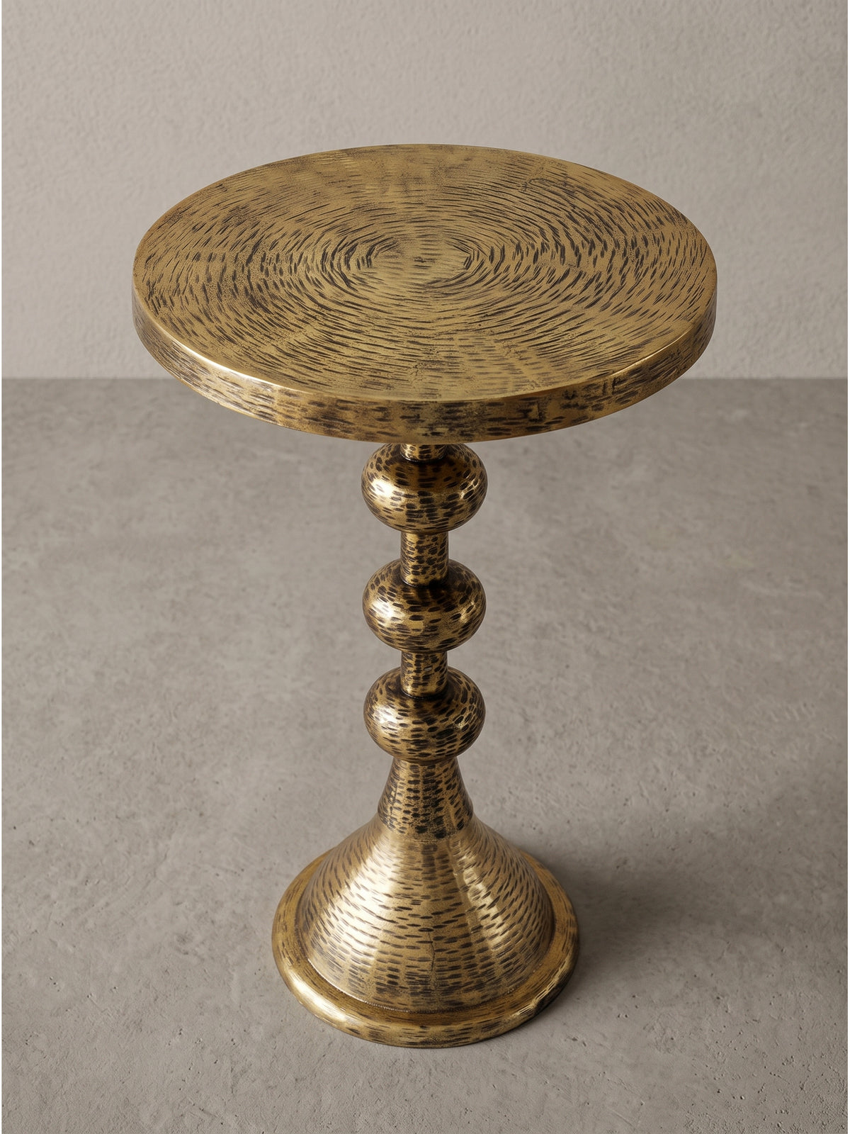 Leicht schräge Ansicht des goldenen Dekotisches, die den glockenförmigen Standfuß und die markant strukturierte Tischplatte im Detail zeigt.