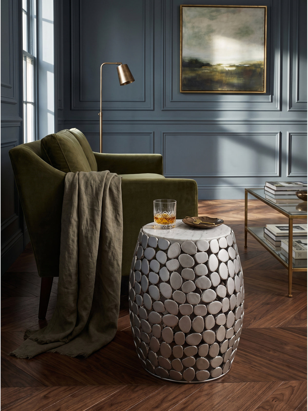 Silberner Metall-Beistelltisch neben einem olivgrünen Sessel auf einem Seidenteppich im eleganten Wohnzimmer_