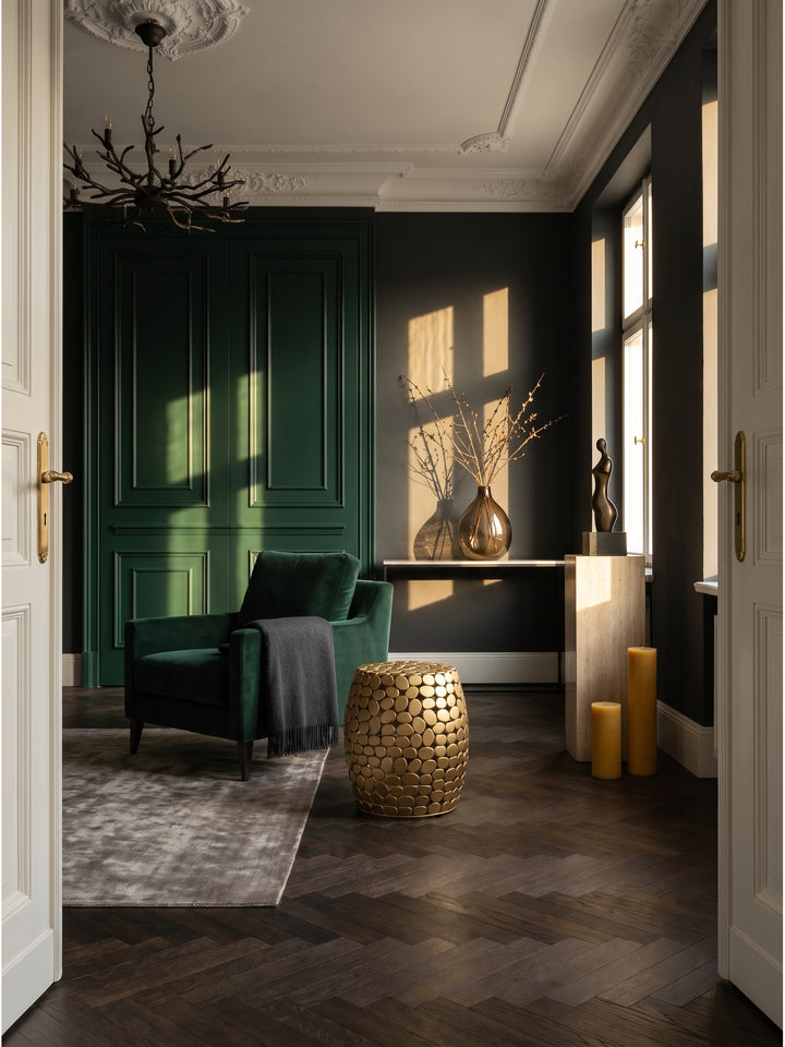 Skulpturaler Beistelltisch aus goldenem Aluminium im luxuriösen Art-Deco Wohnzimmer vor dunkelgrüner Wandvertäfelung._