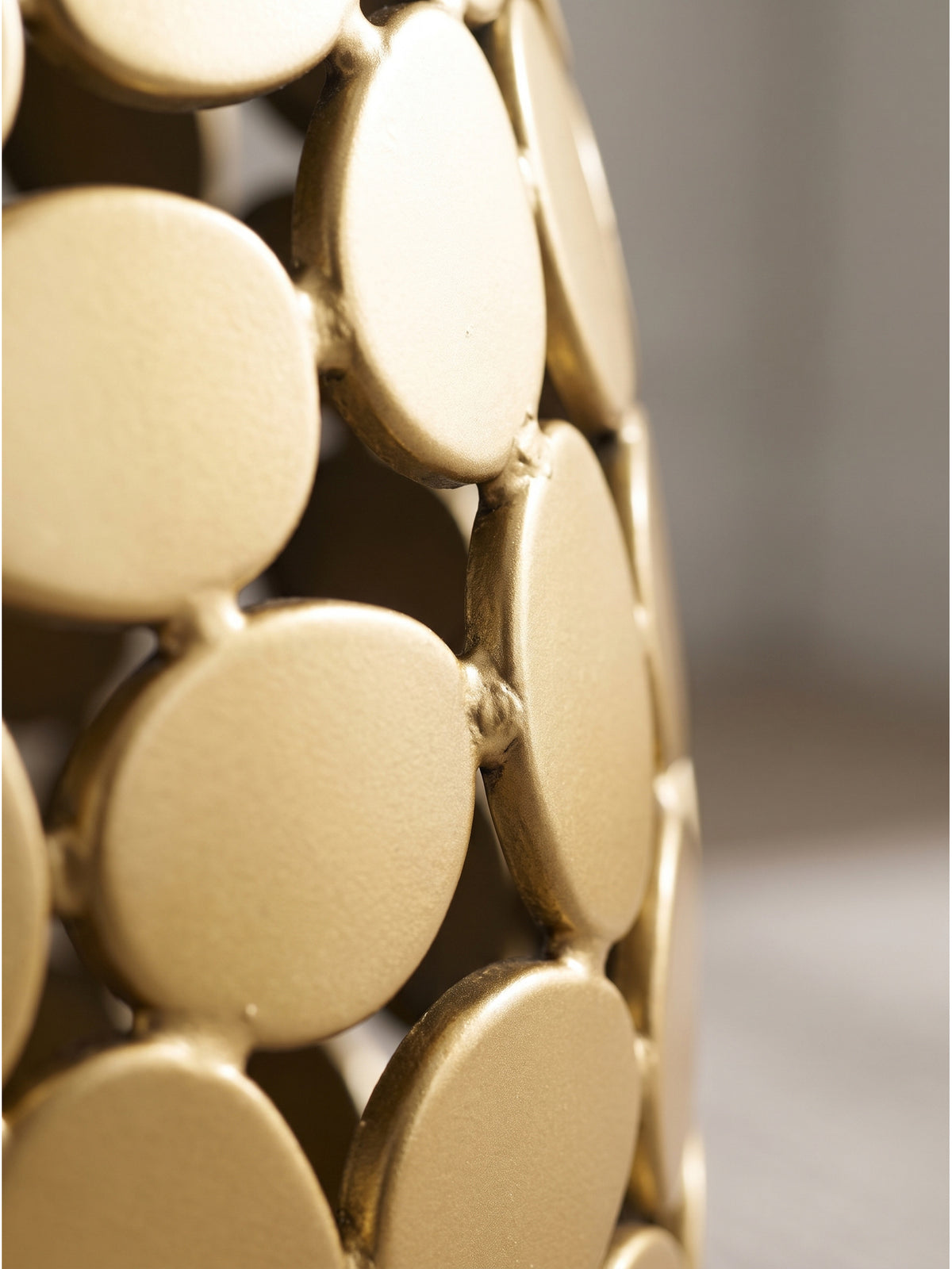 Nahaufnahme der organisch geformten goldenen Aluminium-Elemente und der durchbrochenen Struktur des Design-Beistelltisches._