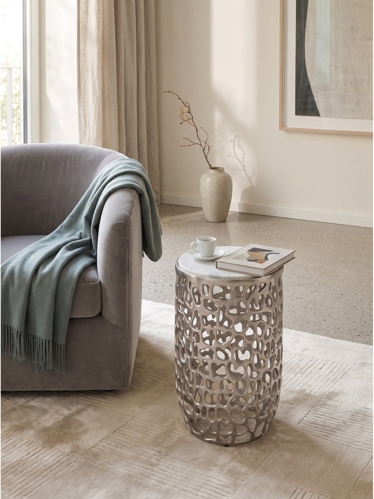 Silberner Metalltisch mit Marmor als skulpturaler Akzent im modern klassischen Wohnbereich neben einem Samtsofa_