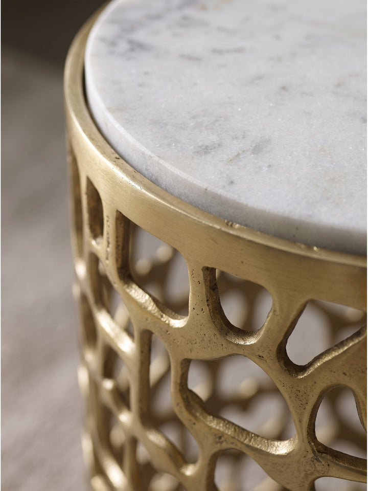 Detailaufnahme der weißen Marmorplatte und des organischen goldenen Aluminiumgestells des Beistelltisches bei warmem Licht_