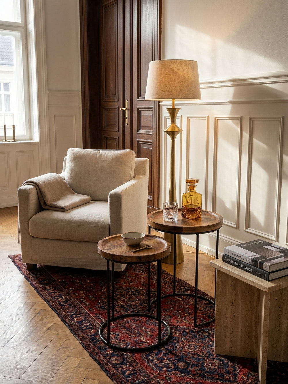 Zwei unterschiedlich hohe Wohnzimmertische aus dunklem Holz und schwarzen Eisenstreben arrangiert vor einem eleganten Samtsofa._