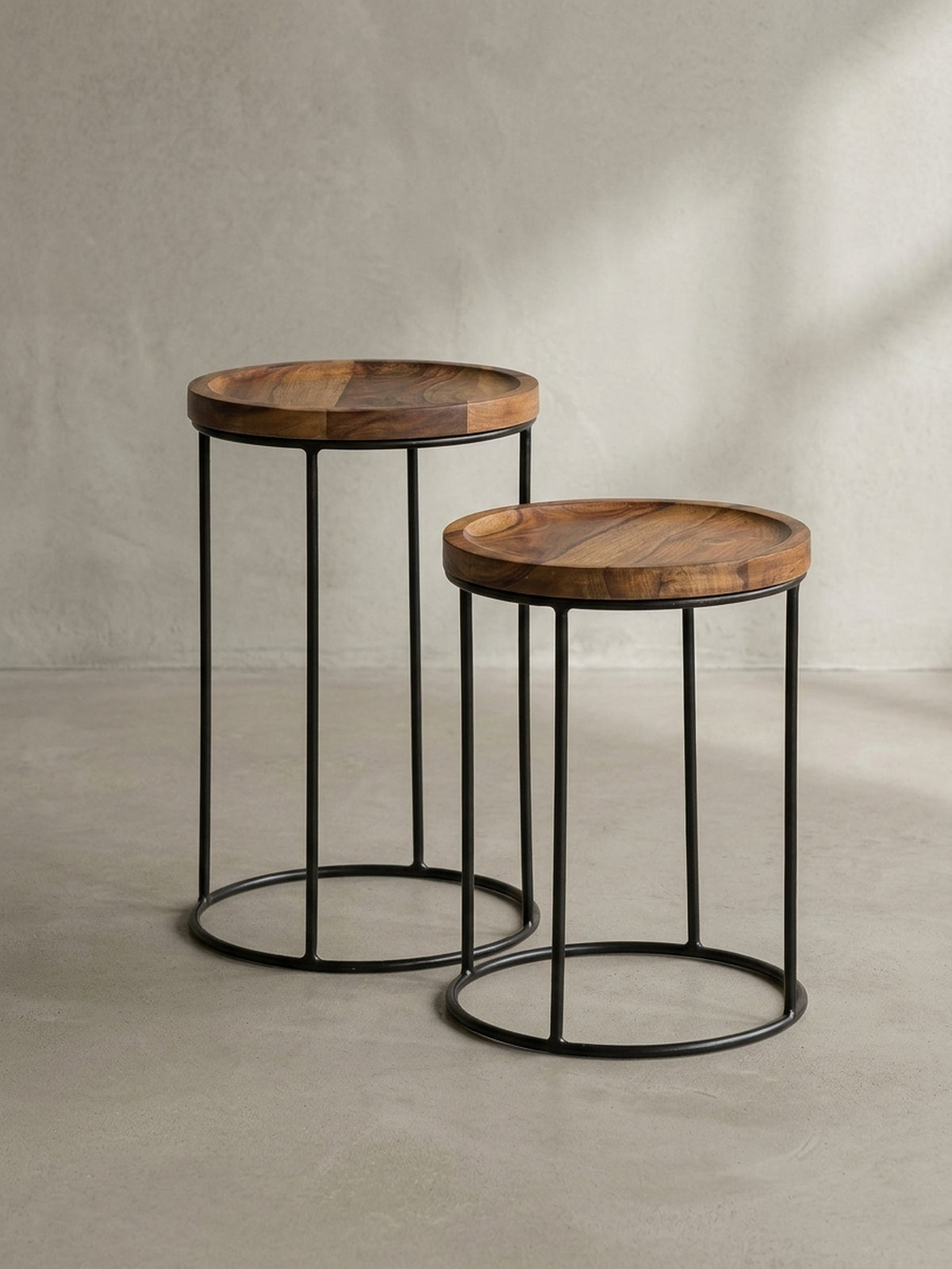 Zwei minimalistische Kaffeetische aus dunklem Massivholz und Eisen zeigen ihre puristische Silhouette vor neutralem Hintergrund._