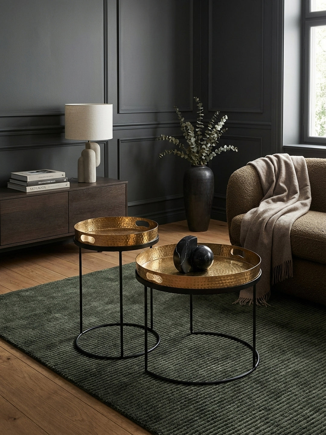 Ein modernes 2er Set Beistelltische mit goldener Hammerschlag-Platte und schwarzem Metallgestell, elegant arrangiert neben einem Sofa in einem stilvollen Wohnzimmer._