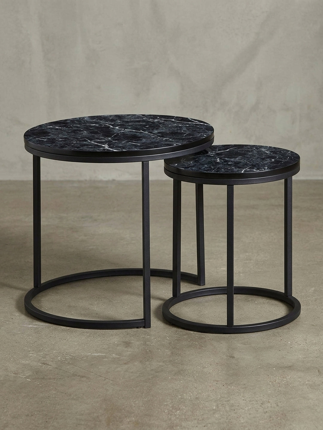 Moderner Satztisch aus einer schrägen 3/4-Ansicht, die die schlanke Struktur des mattschwarzen Stahlgestells und die ineinandergreifende Form der beiden Tische zeigt._