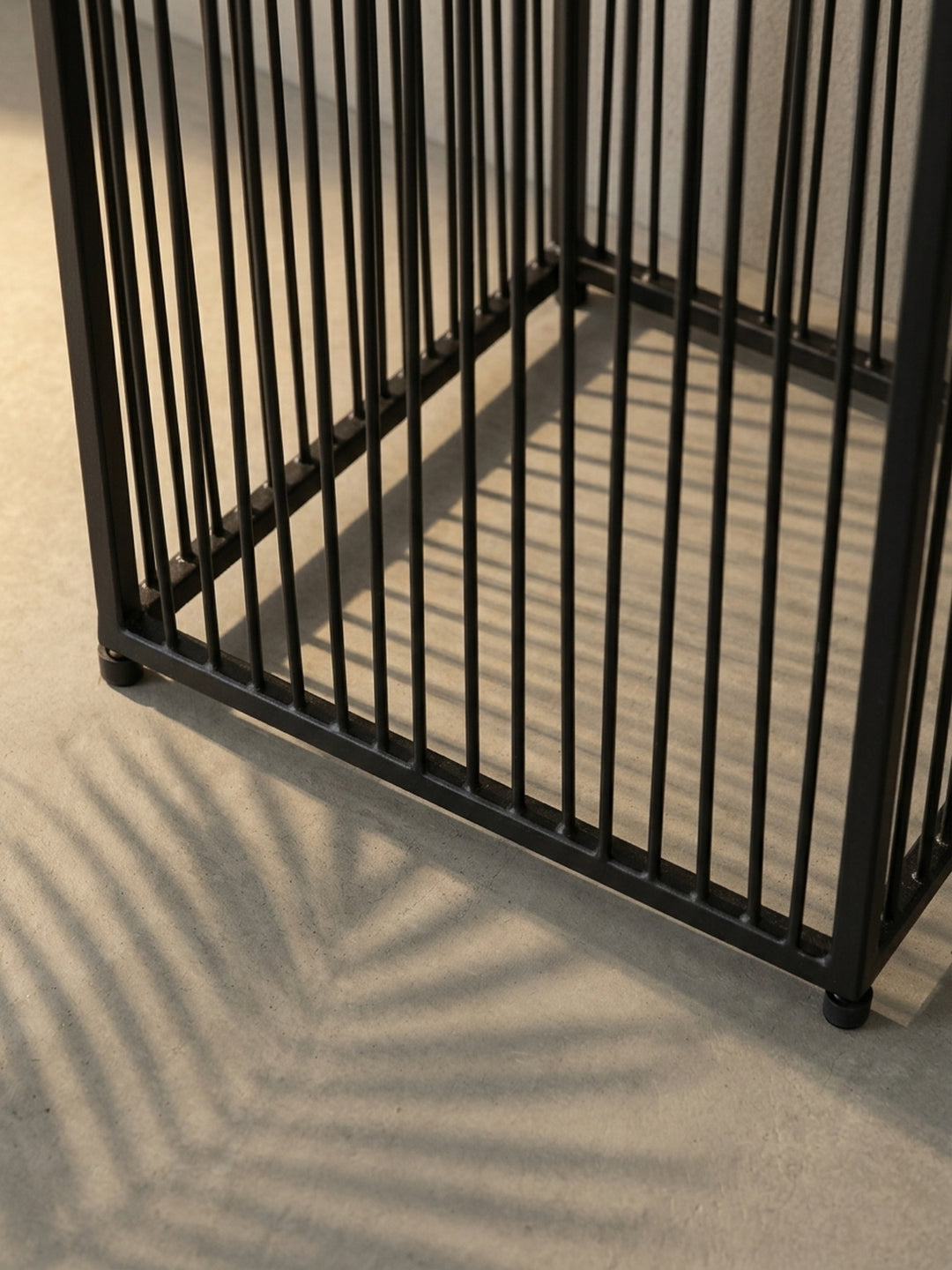 Nahaufnahme des Übergangs vom gerippten Pflanzkasten zum filigranen Stäbchengestell des schwarzen Blumentopfs, ein Detail des modernen Industriedesigns._