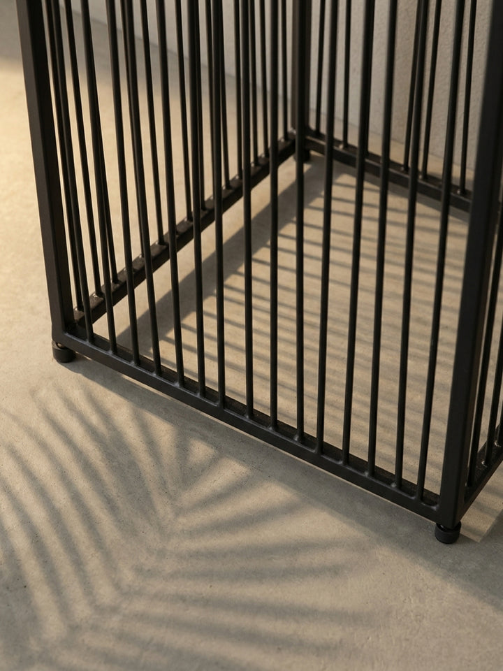 Nahaufnahme des Übergangs vom gerippten Pflanzkasten zum filigranen Stäbchengestell des schwarzen Blumentopfs, ein Detail des modernen Industriedesigns._