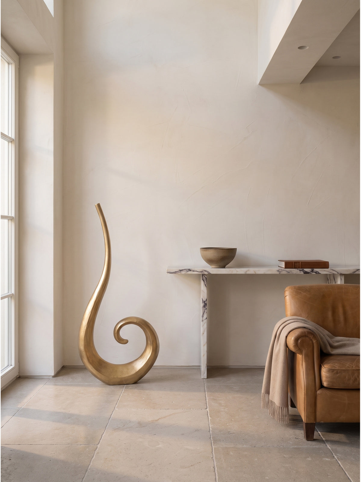 Stilvolle 100 cm große Wohnzimmer-Vase aus Aluminium mit einzelnem Trockenzweig dekoriert vor einer handverputzten warmweißen Tadelakt-Wand_