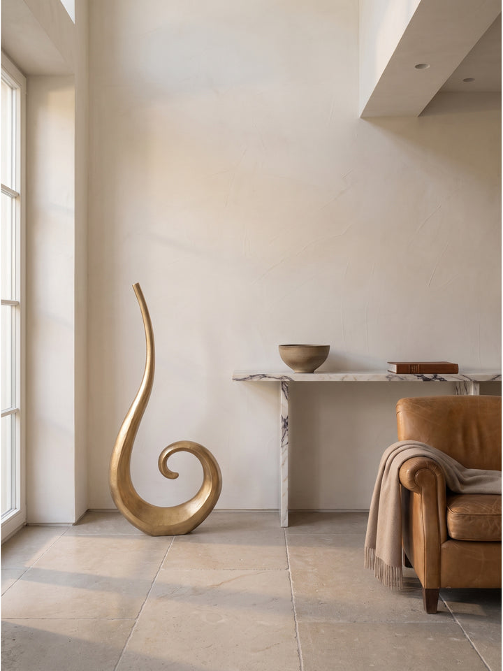 Stilvolle 100 cm große Wohnzimmer-Vase aus Aluminium mit einzelnem Trockenzweig dekoriert vor einer handverputzten warmweißen Tadelakt-Wand_