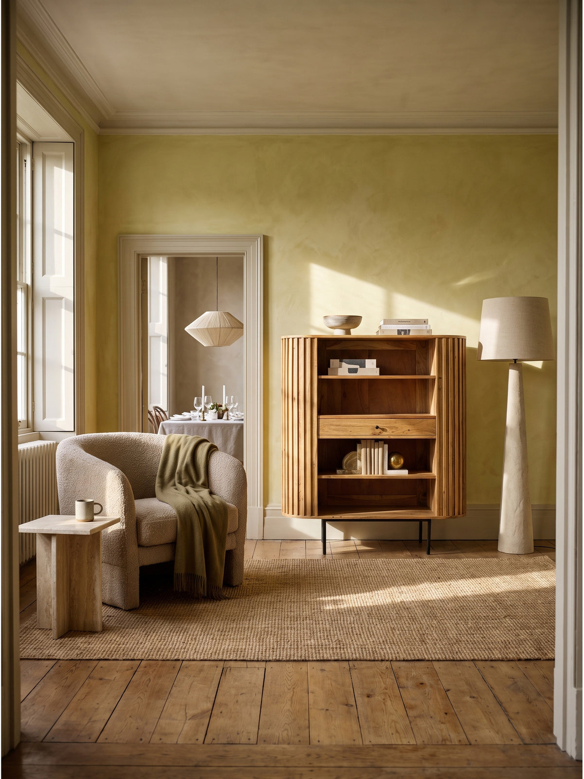 Bücherregal aus massivem Akazienholz mit Lamellen-Design 105x122 cm freistehend im modern eingerichteten Wohnzimmer mit warmweißen Wänden._