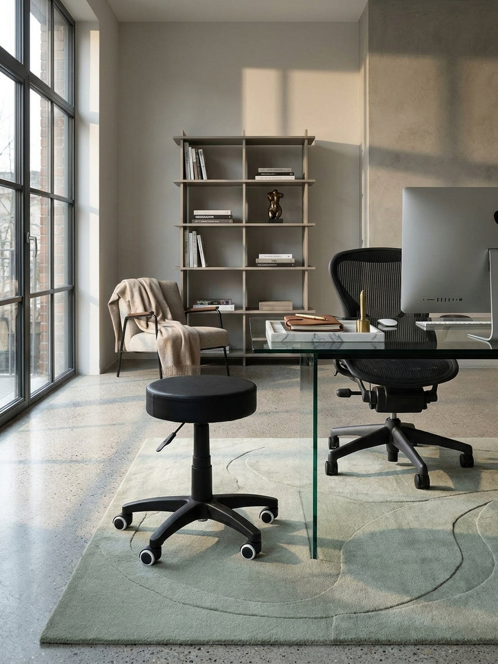 Dieser praktische Praxishocker in Schwarz wird hier elegant mit einem puristischen Glastisch und einem offenen industriellen Stahlregal in einem hellen, professionellen Büro kombiniert._