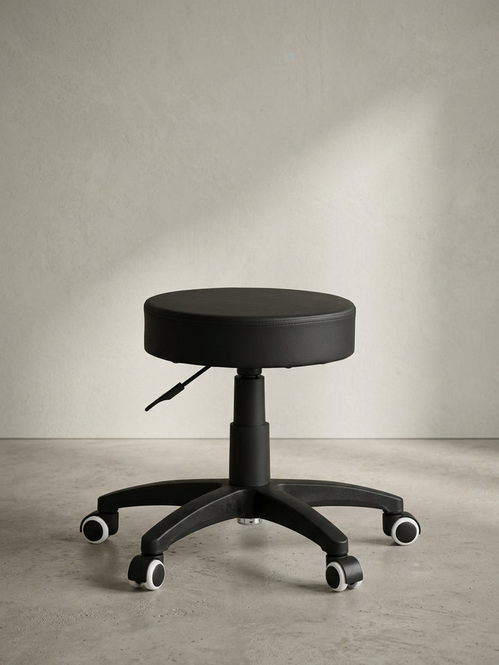 Schwarzer Kosmetikhocker in angewinkelter Perspektive fotografiert, zeigt das puristische und rein auf Funktion reduzierte Design, welches perfekt für den professionellen Arbeitsalltag ist._