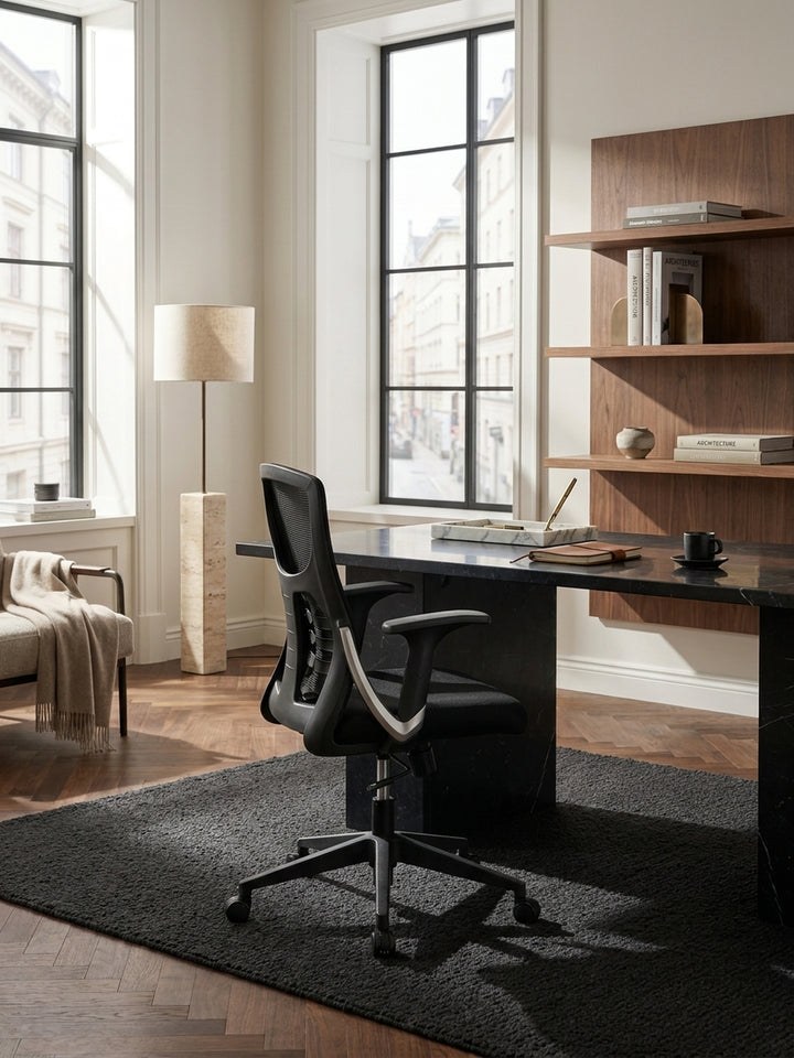 Moderner Schreibtischsessel mit Armlehnen in Schwarz kombiniert mit einem dunklen Massivholz-Schreibtisch und einem puristischen Rollcontainer im Arbeitszimmer._