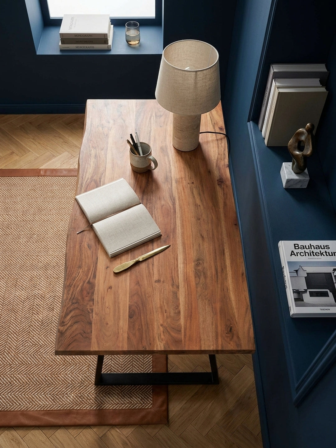 Draufsicht auf einen massiven Holztisch mit schwarzen Metallbeinen, arrangiert mit einem Laptop und Büchern in einem modernen Arbeitszimmer._