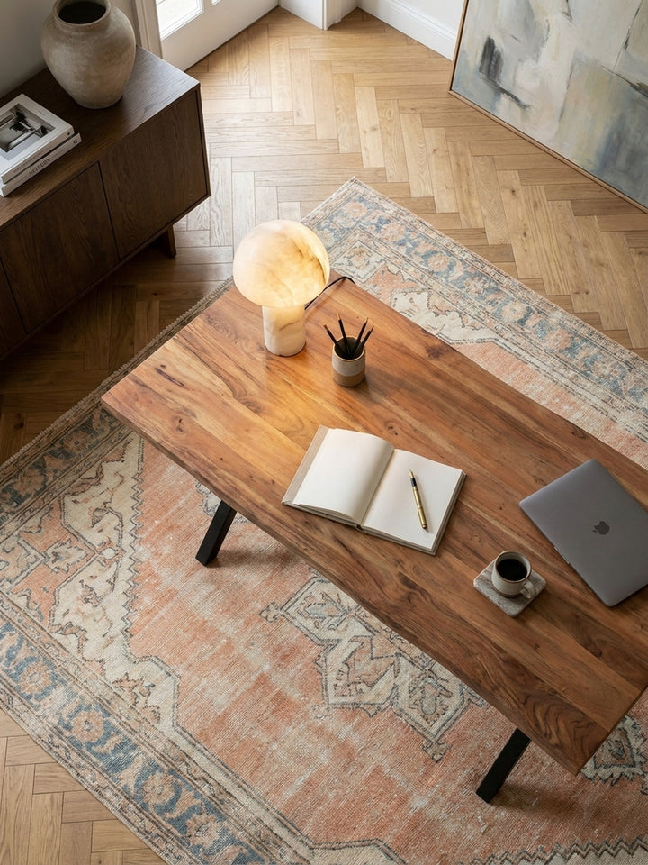 Draufsicht auf den massiven Akazie-Schreibtisch mit Baumkante, der zentral auf einem Vintage-Teppich im stilvoll eingerichteten Arbeitszimmer platziert ist._