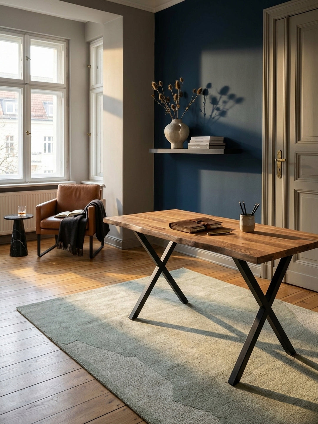 Eleganter Homeoffice-Arbeitsplatz mit einem Schreibtisch aus massivem Akazienholz und schwarzen X-Beinen auf einem Vintage-Perserteppich in einem lichtdurchfluteten Altbau-Arbeitszimmer._